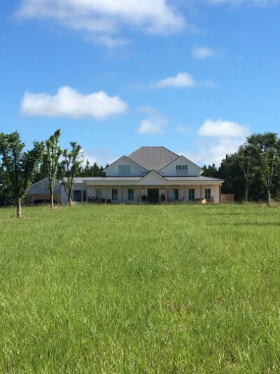 Wide front yard of a white house with rib granite roofing